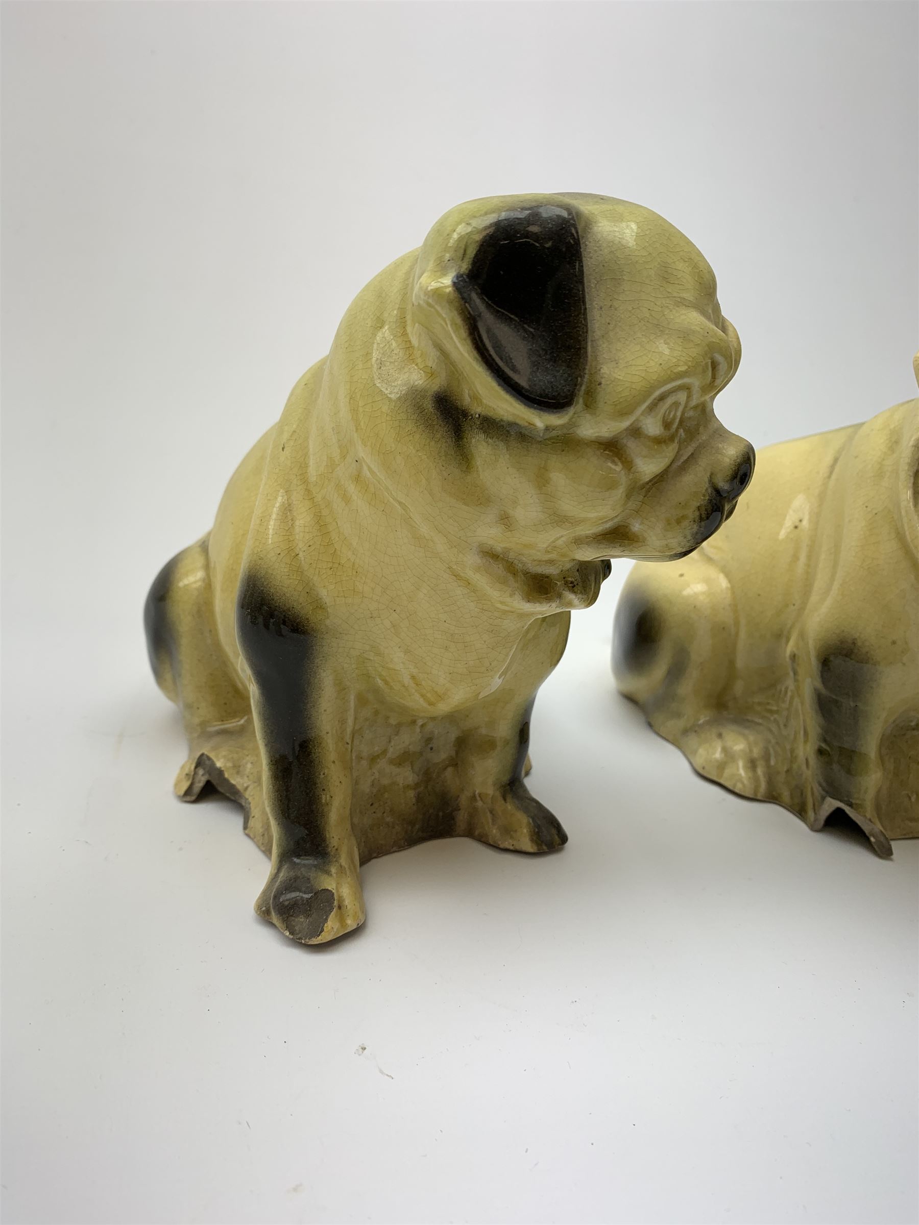A collection of various ceramic figurines, to include pair of small 19th century Staffordshire cats, Royal Doulton cat, Coalport cat, pair of 19th century pug dogs, two fairings inscribed Good Templars, two Bonzo dog peppers, a number of pin cushion dolls, various 20th century and later black pottery cats, Victorian bisque figures, etc. 