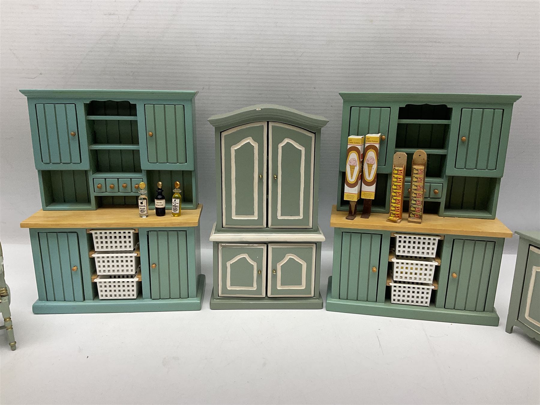 Collection of miniature dolls house furniture, to include display cabinet with pink and white floral dinner service, two serving trolleys with cakes and sweets and two blue painted kitchen dressers, together with miniature dolls house cardboard food packaging and animal figures including dogs and cats, etc