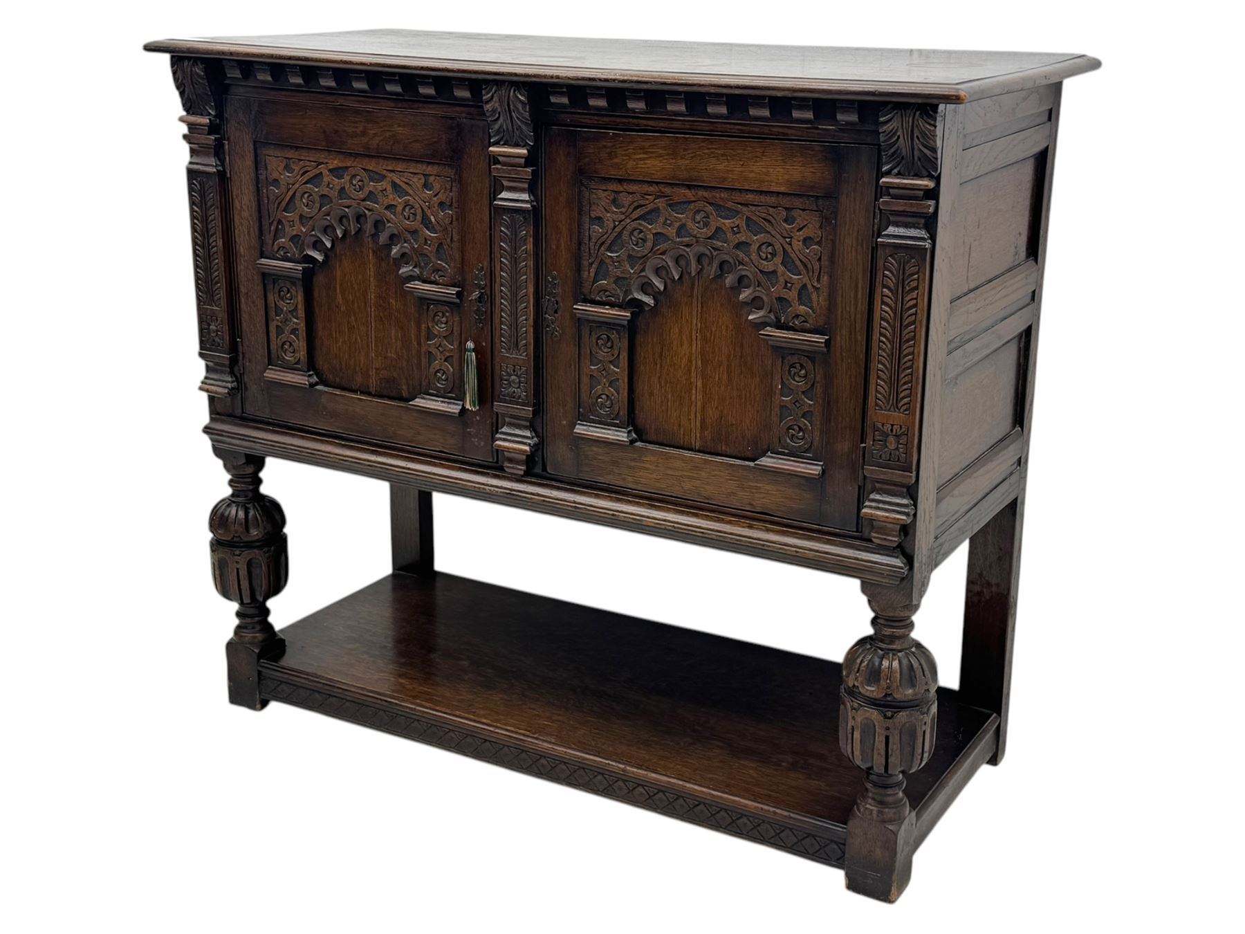 Jacobean design carved oak two door cupboard, the frieze and twin cupboard doors carved with arcaded panels and stylised foliage, raised on baluster supports united by an undertier