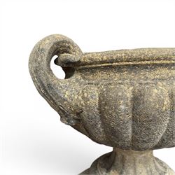 Pair of Neoclassical design weathered cast stone garden urns of kylix form, the rolled rim flanked by twin pierced scroll handles over a shallow gadrooned bowl, raised on a fluted circular socle and faux panelled square pedestal base