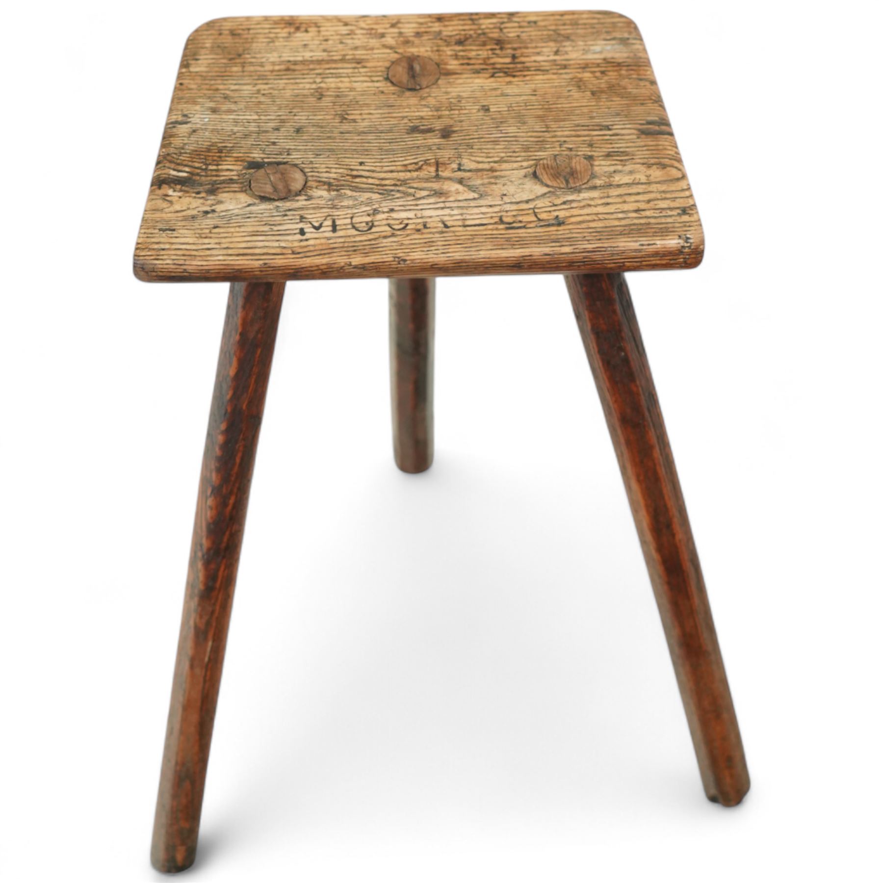 19th-century Sheffield type Cutler's stool, in elm and ash, with a solid rectangular seat, chamfered underside, on three wedge tenoned chamfered legs, the top of the seat with indistinct carved lettering