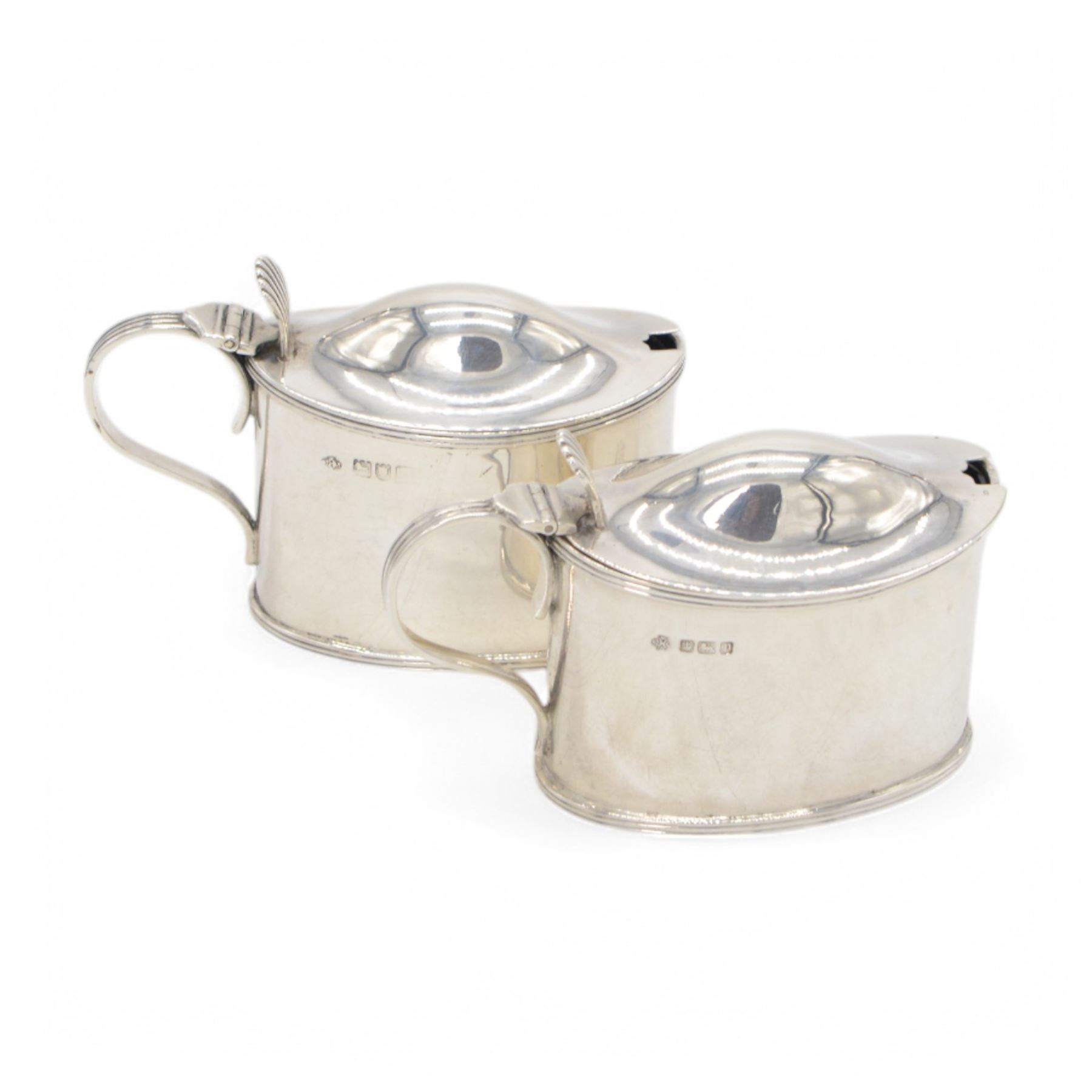 Pair of Edwardian silver mustard pots, of oval form with reed borders and palmette thumb pieces to hinged covers, opening to reveal blue glass liners, hallmarked William Hutton & Sons Ltd, London 1905, H7.5cm