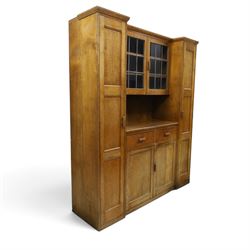Arts & Crafts oak housekeeper’s cupboard, stepped moulded cornice over twin leaded glazed doors enclosing shelved interior, flanked by narrow panelled cupboards, open recess below over two drawers and twin panelled cupboard doors, with rectangular handles