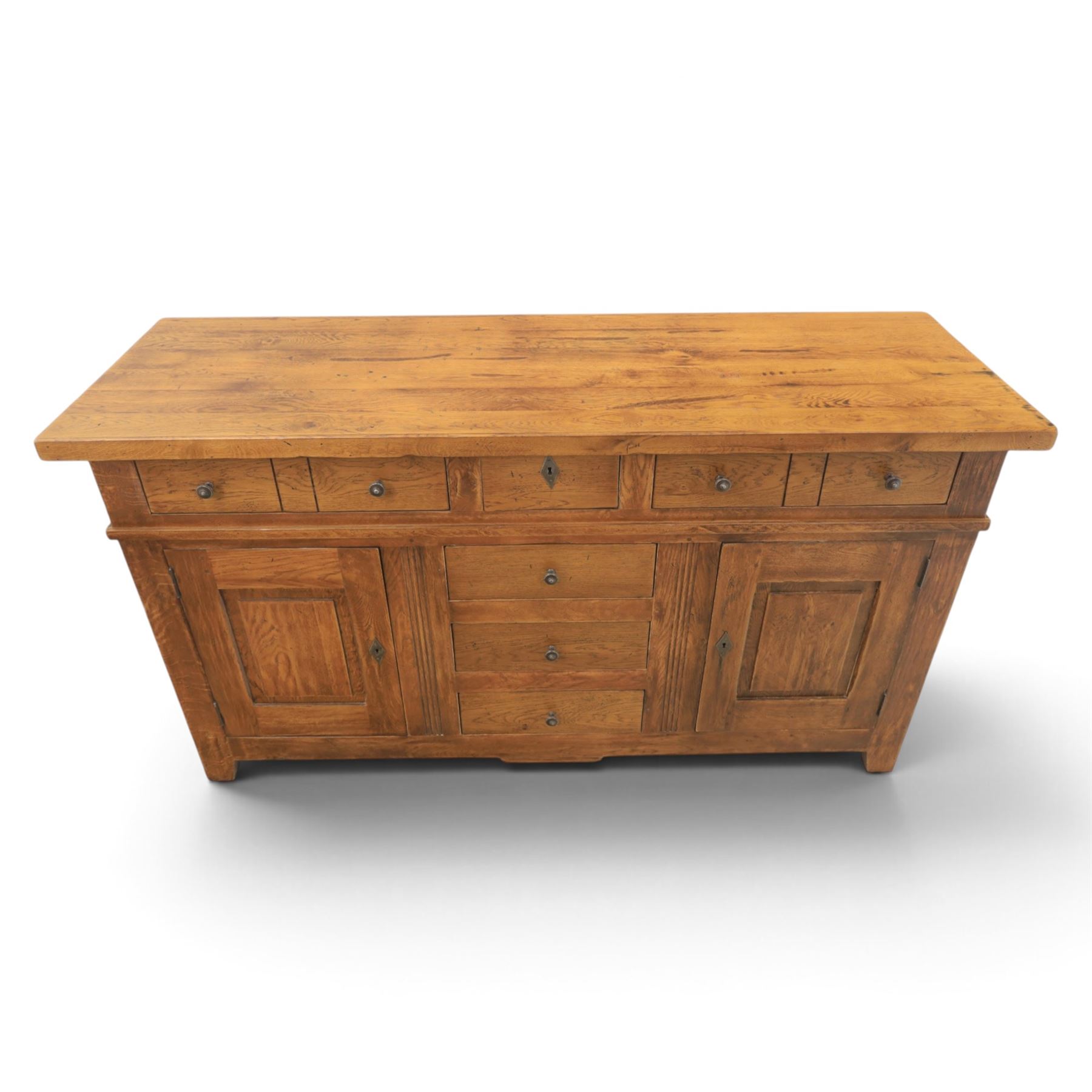 Indigo Furniture - large rustic oak sideboard fitted, with three drawers above three central drawers, flanked by fielded panelled doors, raised on bracket feet