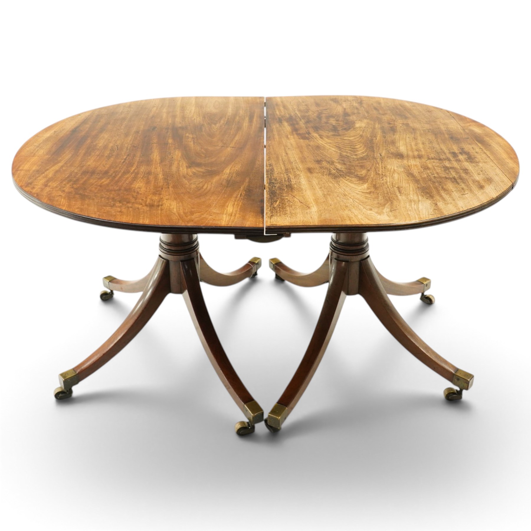 George III mahogany twin pedestal extending dining table, the twin D-ends with additional leaf, raised on twin turned pedestals terminating to four splayed supports with brass cups and castors
