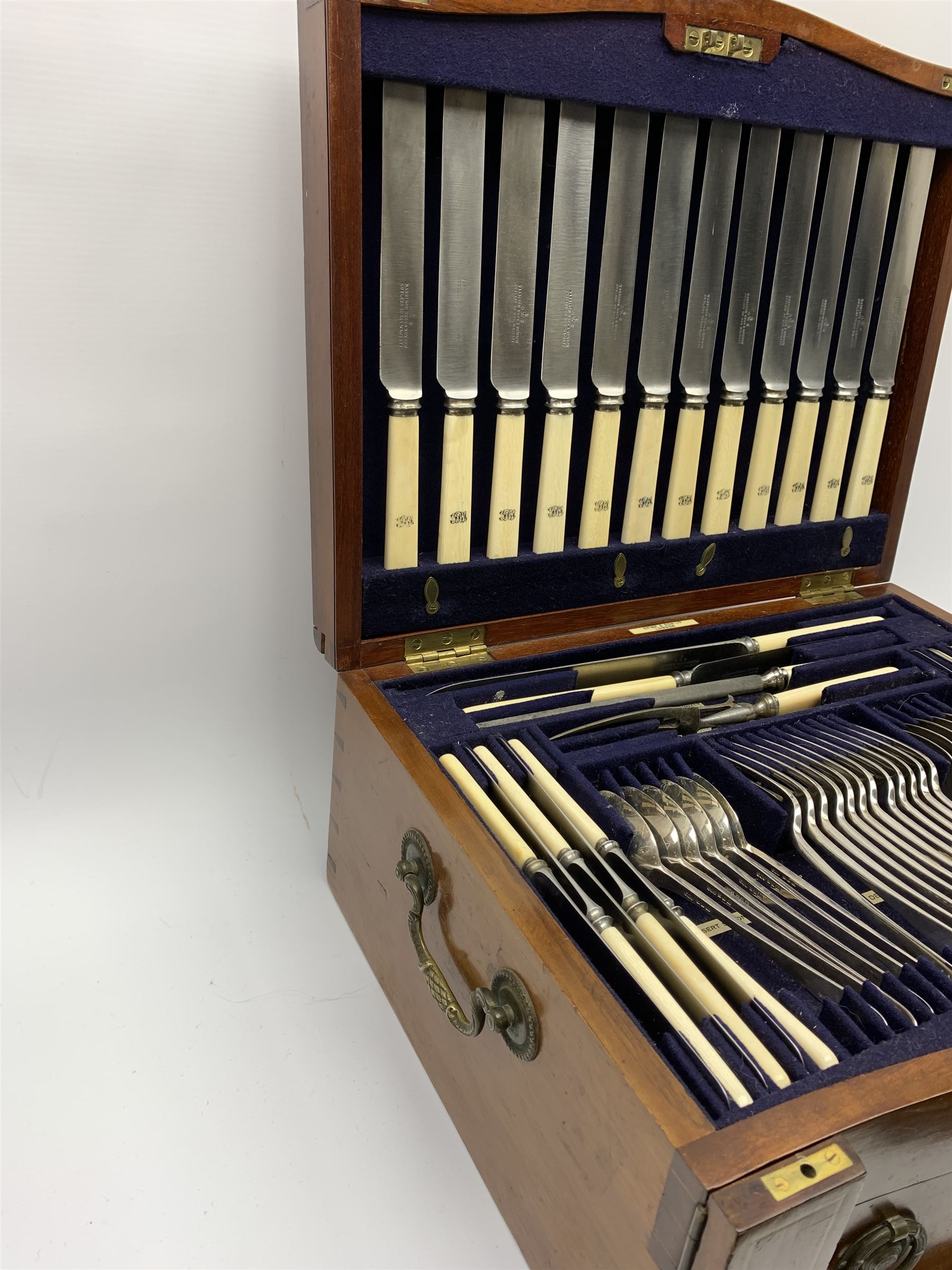 Late 19th/early 20th century composite canteen of silver flatware, contained within an early 20th century mahogany serpentine fronted case with twin drop carry handles, and hinged cover with boxwood stringing and central inlaid shell motif, above a single drawer with twin ring handles and Wellington style locking system, the cover and drawer opening to reveal plaque for Spink & Sons Ltd London, and fitted interior containing ivory handled knives, ivory handled carving set, and silver Hanoverian and Old English pattern cutlery, each with engraved monogram to terminal, hallmarked London, makers Spink & Son (John Marshall Spink), Goldsmiths & Silversmiths Co, and Chawner & Co (George William Adams), various dates ranging 1880-1923, gross weighable silver 92.59 ozt (2880 grams)