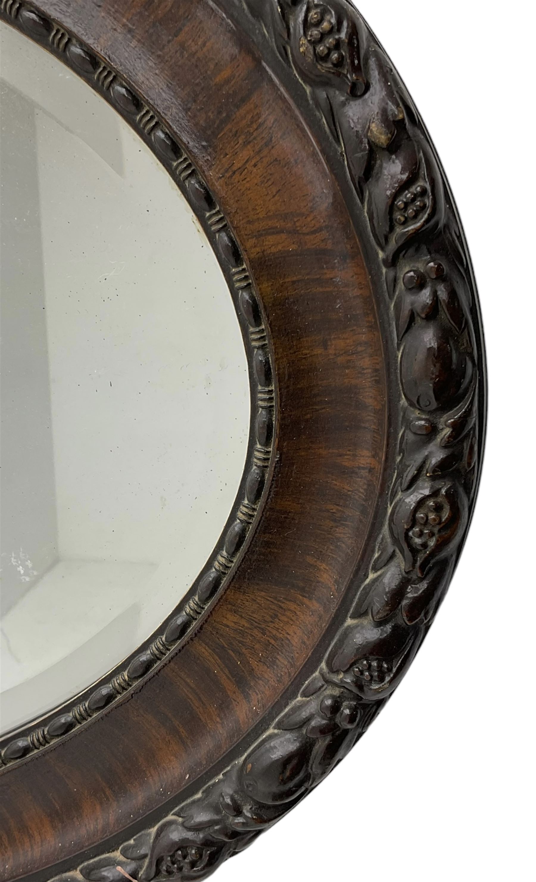 Early 20th century oval mirror, moulded frame decorated with trailing foliage and berries, bevelled plate