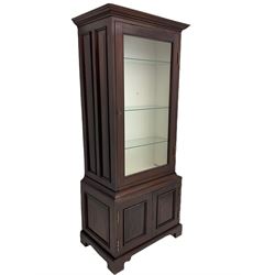 Mahogany display cabinet with hidden compartment, projecting cornice over single glazed door enclosing glass shelves, double panelled cupboard below, the interior with button releasing sliding back compartment, on bracket feet