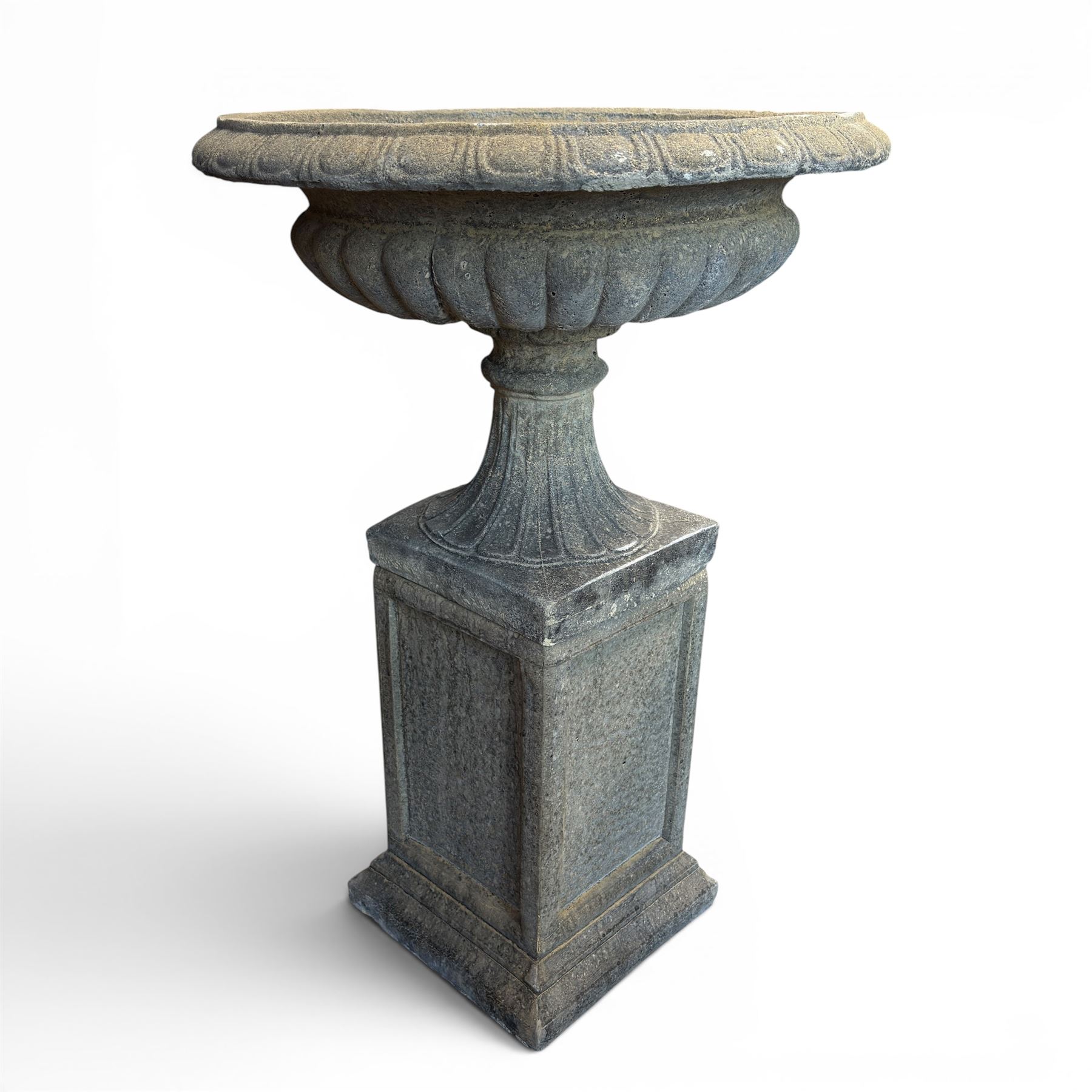 Pair of cast stone garden urns of kylix form on pedestals, the broad egg-and-dart moulded rim over a shallow gadrooned underbelly, with waisted tapering base, raised on matching plinth bases with faux panelled facia