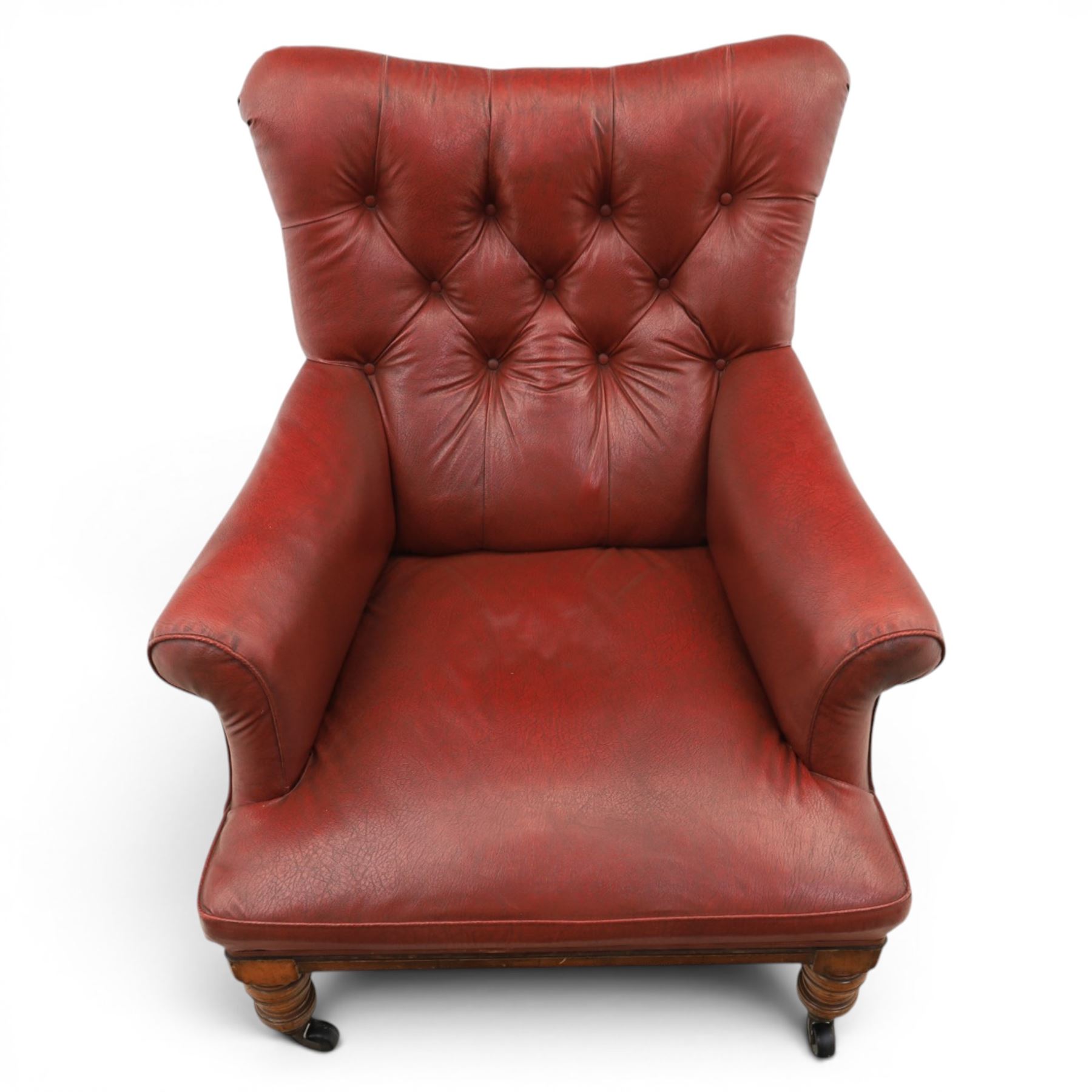 Early 20th century style oxblood red leather Chesterfield armchair, deep buttoned shaped back over padded scroll arms and loose seat cushion, raised on turned mahogany front supports with brass caps and castors