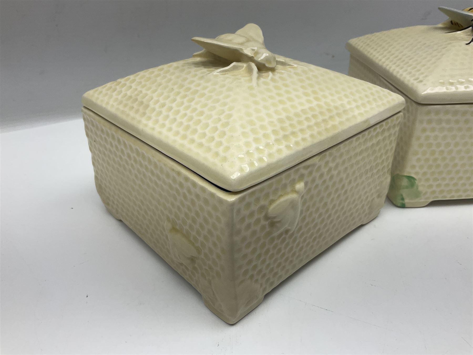 Four square honey boxes with lids,  each decorated with honeycomb pattern and finished with a bee finial