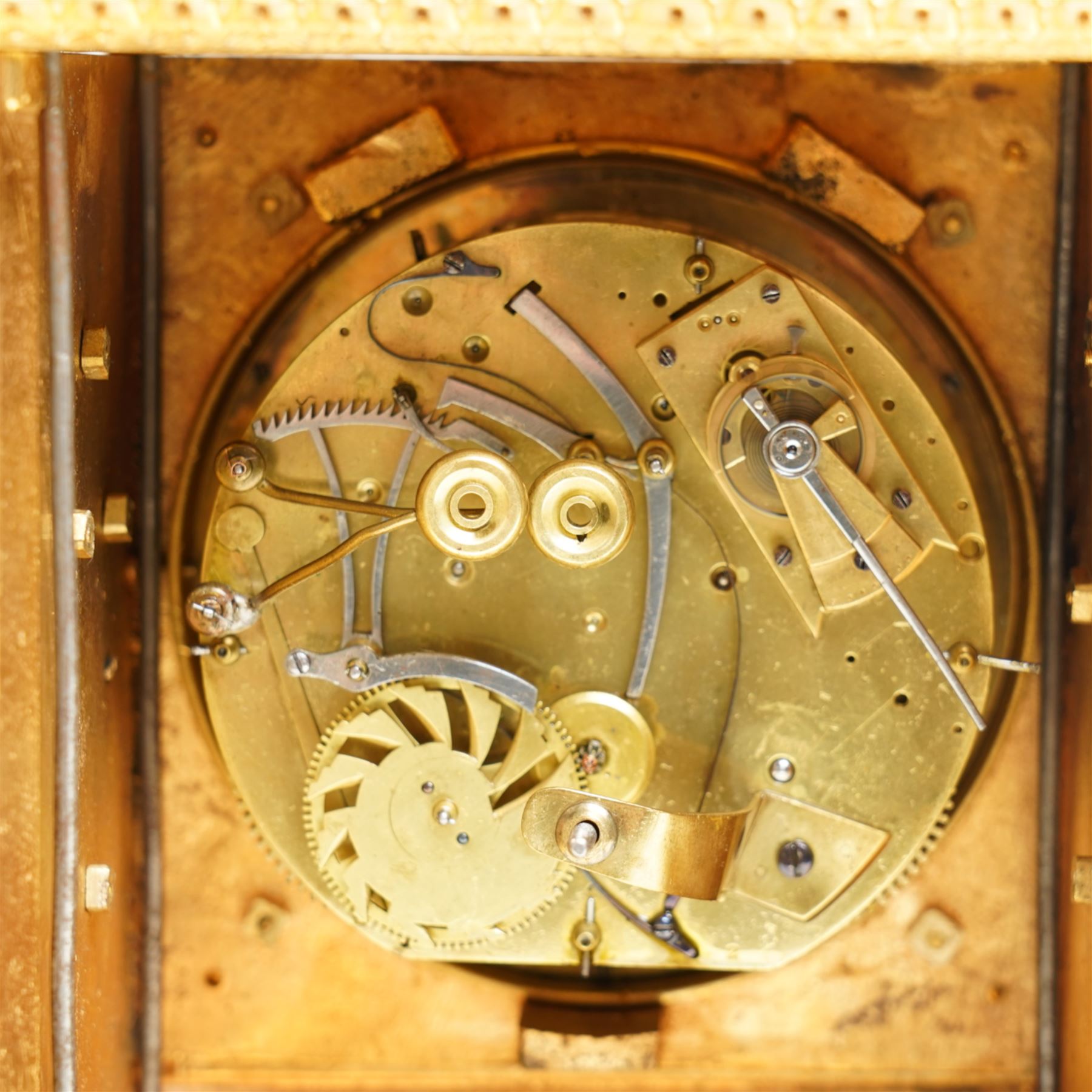 Fine Swiss ormolu 8-day early 19th century Pendule d'Officer style clock c1820,  circular double train ting-tang movement striking the quarters on a graduated pair of bells and sounding the hour on one, going train with a vertical platform lever escapement and over sprung balance, rack striking, with visible hour and quarter strike work to the backplate, movement unsigned, convex enamel dial with Roman numerals and steel moon hands behind a glazed gilt bezel, case with a scroll cast handle to the arched top with applied rococo decoration to the tympanum, both sides of the case adorned with a military trophy of arms motif and deep frieze with foliate arcading beneath, on a rectangular plinth with decorative scroll engraved bracket feet. With Key.   