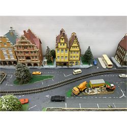 Table top 'N' gauge continental scenic layout as a split level town with various loops of track, station with numerous platforms, engine shed, assorted buildings, roads with motor vehicles and figures, tunnels, trees, river with bridge, tram depot etc 122 x 52cm