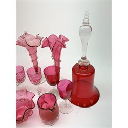 Three Victorian cranberry glass trumpet vases, each with spiralling frilled or crimped decoration, largest H24cm, together with two large Victorian cranberry glass bells, with clear glass handles, H32cm, and a selection of other cranberry glass, comprising bowl, two jugs, and five drinking glasses. (Qty). 
