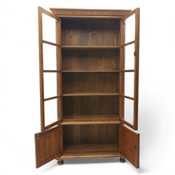 Pair of late 20th century Thai hardwood display cabinets, each with moulded cornice over twin glazed doors enclosing adjustable shelves, panelled cupboard doors below flanked by fluted columns, raised on bun feet