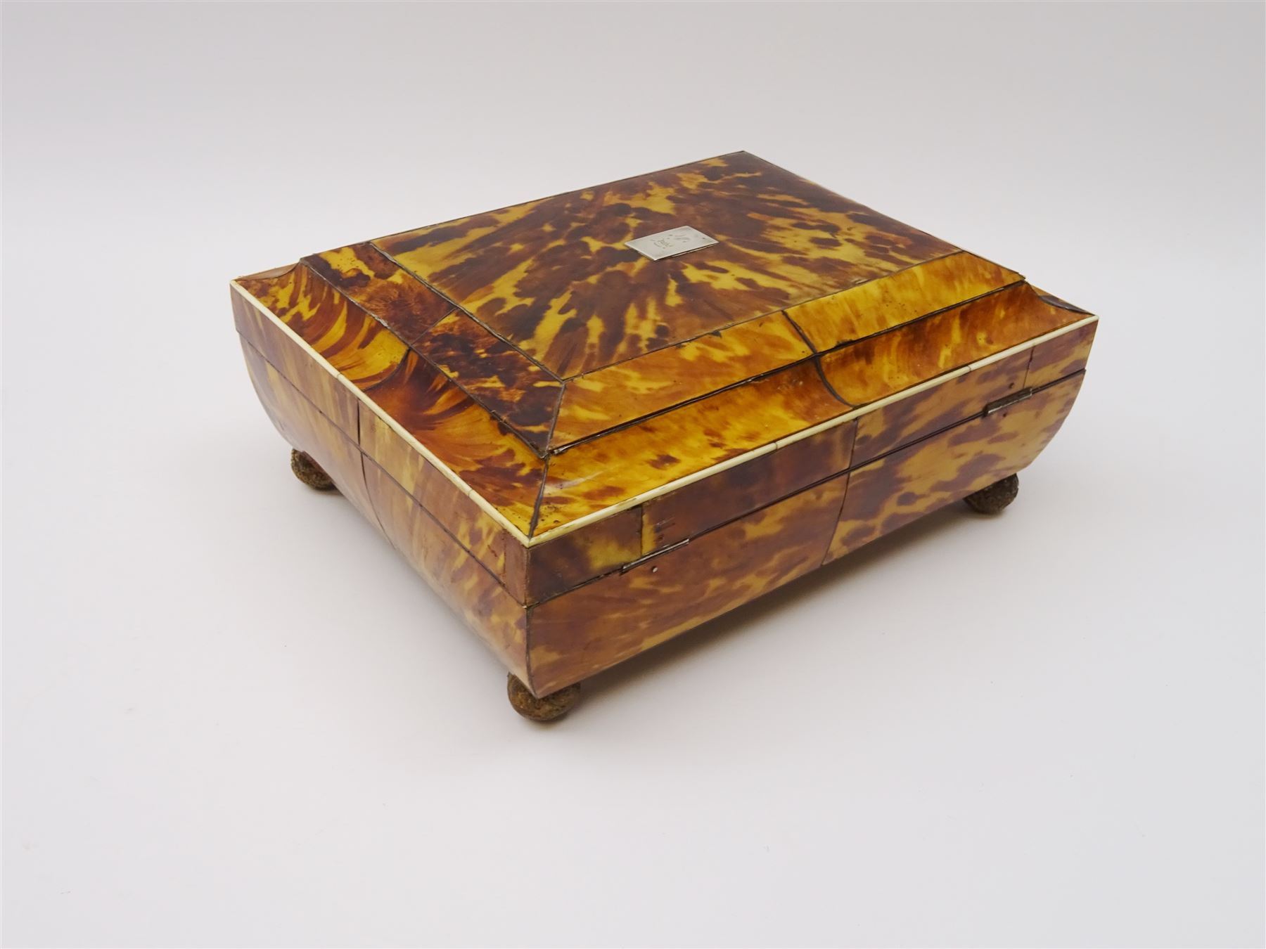 19th century tortoiseshell sewing box, of sarcophagal form upon four foliate detailed brass ball feet, the hinged cover edged in ivory with initialled silver plaque to centre, opening to reveal a silk lined interior, H9.5cm W22.5cm D18cm
