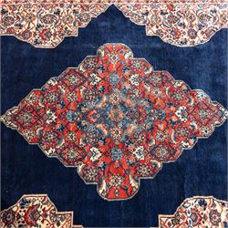 Large West Persian Bidjar hand-knotted carpet, deep indigo field with central medallion with pendants issuing an all-over design of scrolling vines, palmettes, and floral sprays, within conforming spandrels, enclosed a broad madder red palmette, and vine border framed by guard stripes, in a palette, of indigo, madder red and ivory tones, with cotton fringe ends 