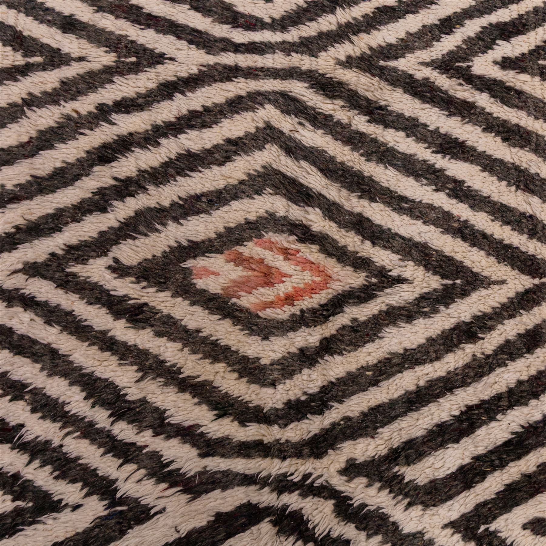 Moroccan Berber hand-knotted rug, of rectangular form, ivory ground decorated with bold, repeating lozenge motifs defined by alternating charcoal grey linear bands, with a striking geometric lattice and chevron with diamond designs, enclosing smaller stylized devices in soft blush tones, with fringe ends