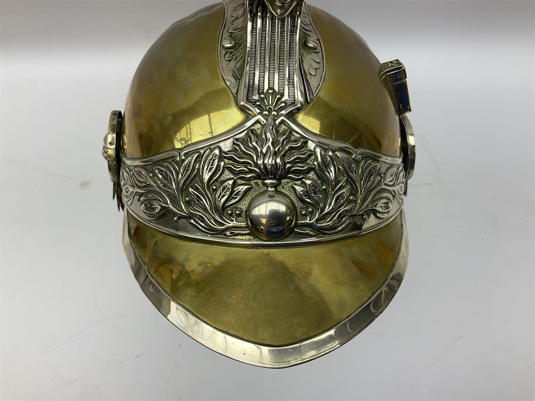 Early 20th century French mounted gendarme's helmet, brass with nickel-silver mountings, broad band embossed with fused grenade, high comb with the face of the gorgon Medusa at the peak and with a black horse hair crest, plume socket at the left, leather-backed nickel-silver chin scales with lion mask mounts.