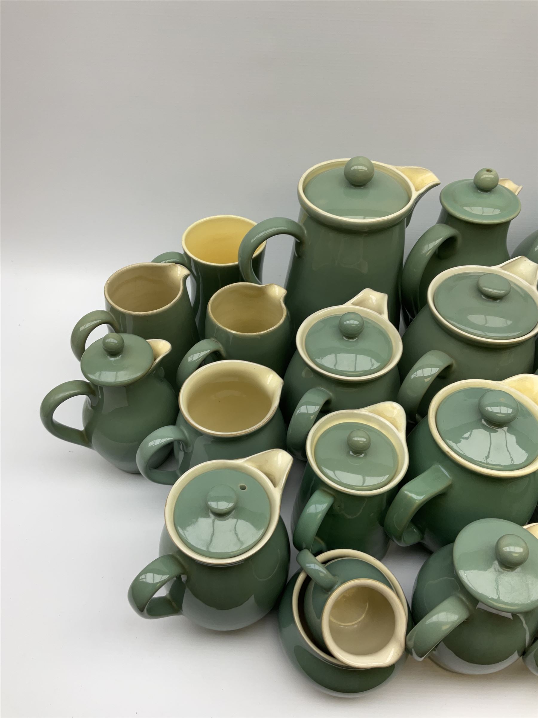 Denby Manor Green pattern tea service, comprising of three teapots, twelve coffee pots of various sizes, four hot water jugs with lids, seven jugs, eleven teacups, four mugs, seventeen saucers, six sugar bowls, two sugar bowls with lids and eleven side plates.  