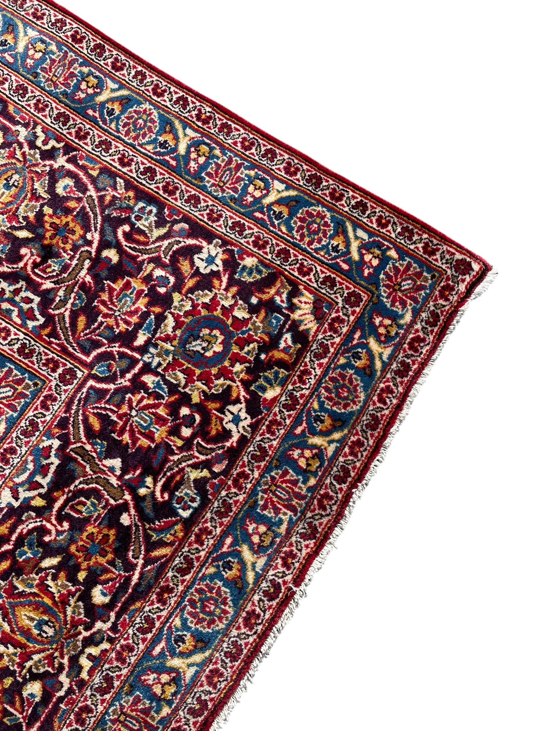 Large Persian Kashan crimson ground carpet, large floral central medallion surrounded by trailing branches decorated with leaves and stylised plant motifs, the main border with scrolling design interspersed with palmettes, within floral pattern guard stripes 