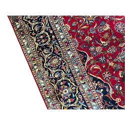 Persian Kashan crimson ground carpet, the central pole medallion decorated with flower heads, surrounded by trailing leafy branches and palmettes, scrolling border decorated with further palmettes, within floral pattern guard stripes 