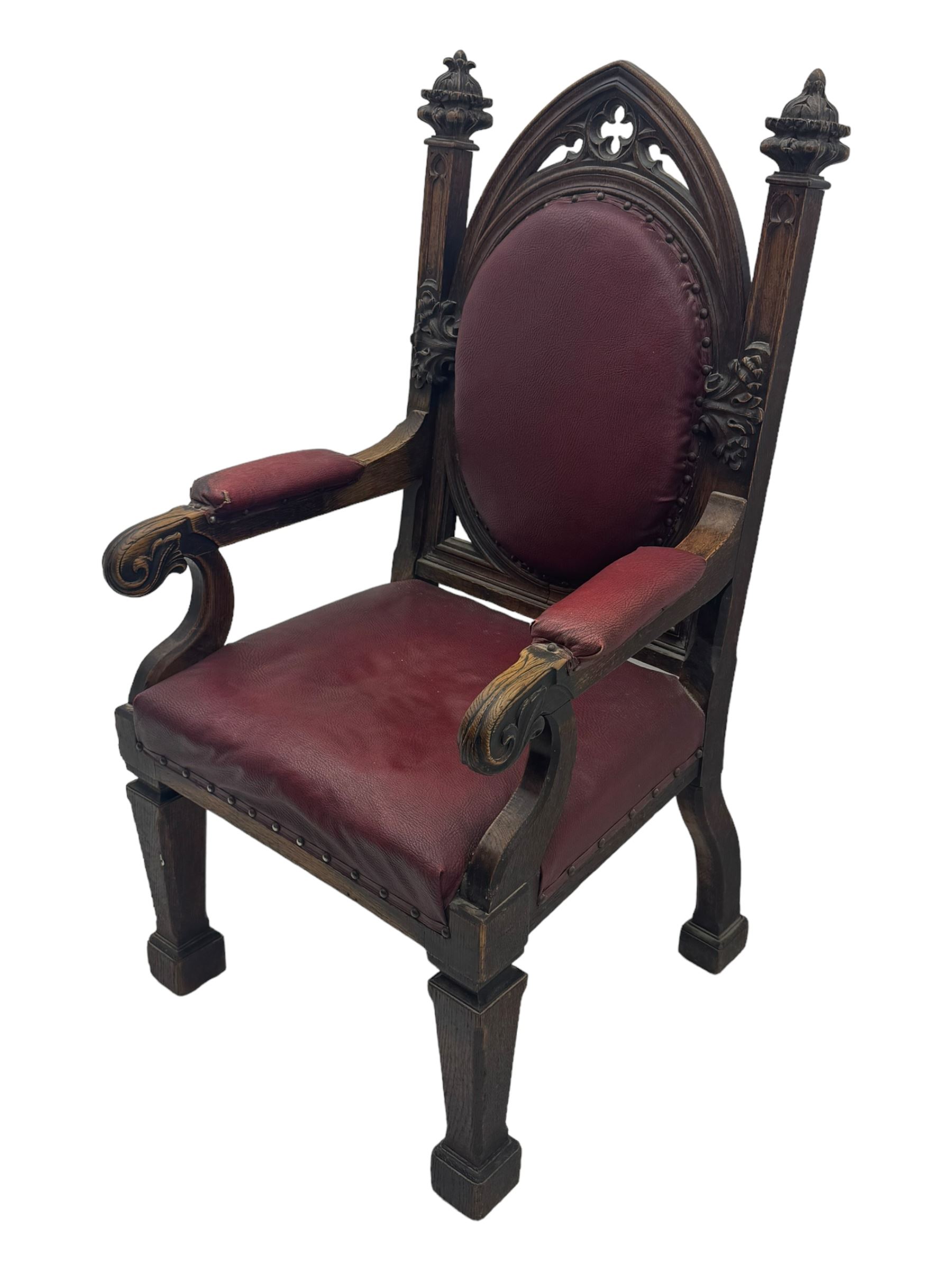 Late Victorian Gothic-revival armchair, arched crest rail carved with tracery and trefoil detail, padded circular back and seat, brass studded burgundy leather upholstery, shaped armrests with scrolled terminals, on square tapering supports