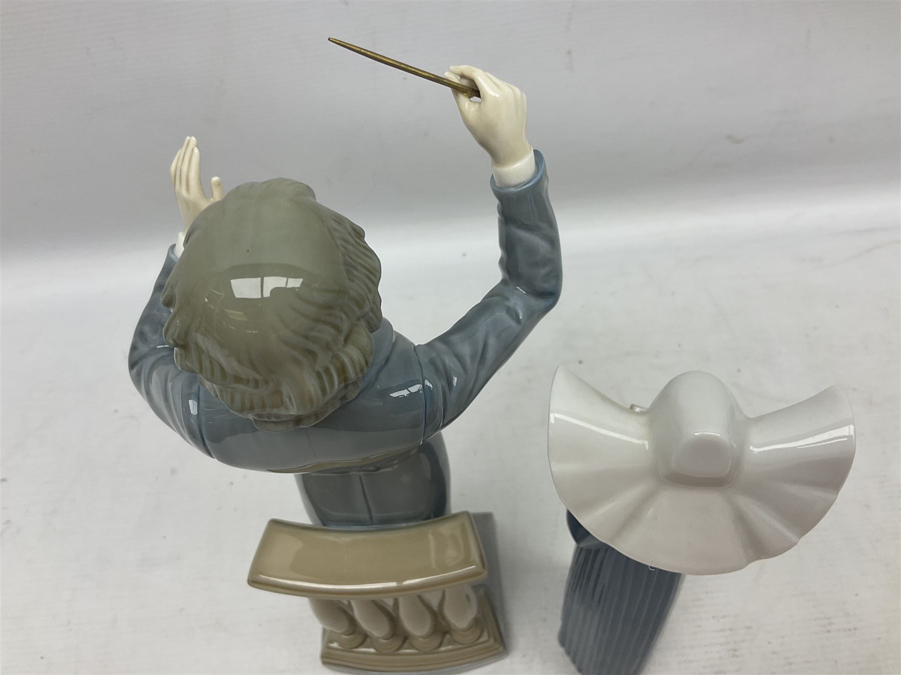 Two Lladro figures, comprising Conductor no 5196 and Prayerful Moment no 5500 together with a Lladro plaque and two Lladro candle holders, Dolphins at Play no 17666 and Sailing the Seas no 17665, all with original boxes, largest example H33cm 