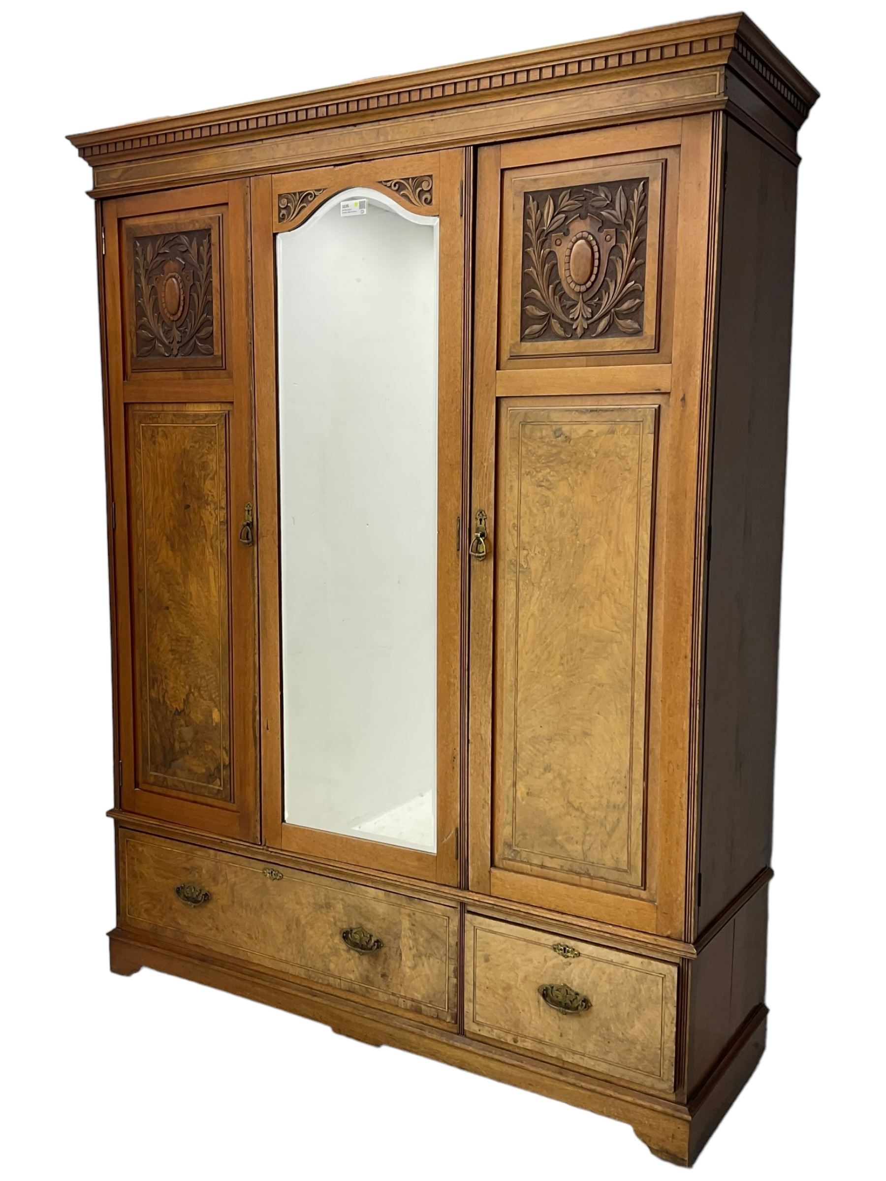 Late Victorian walnut triple combination wardrobe, projecting moulded and dentil cornice, central shaped bevelled mirror glazed door, cartouche and curled leaf carved panels over figured walnut veneered panels, fitted with drawer to base, on bracket feet