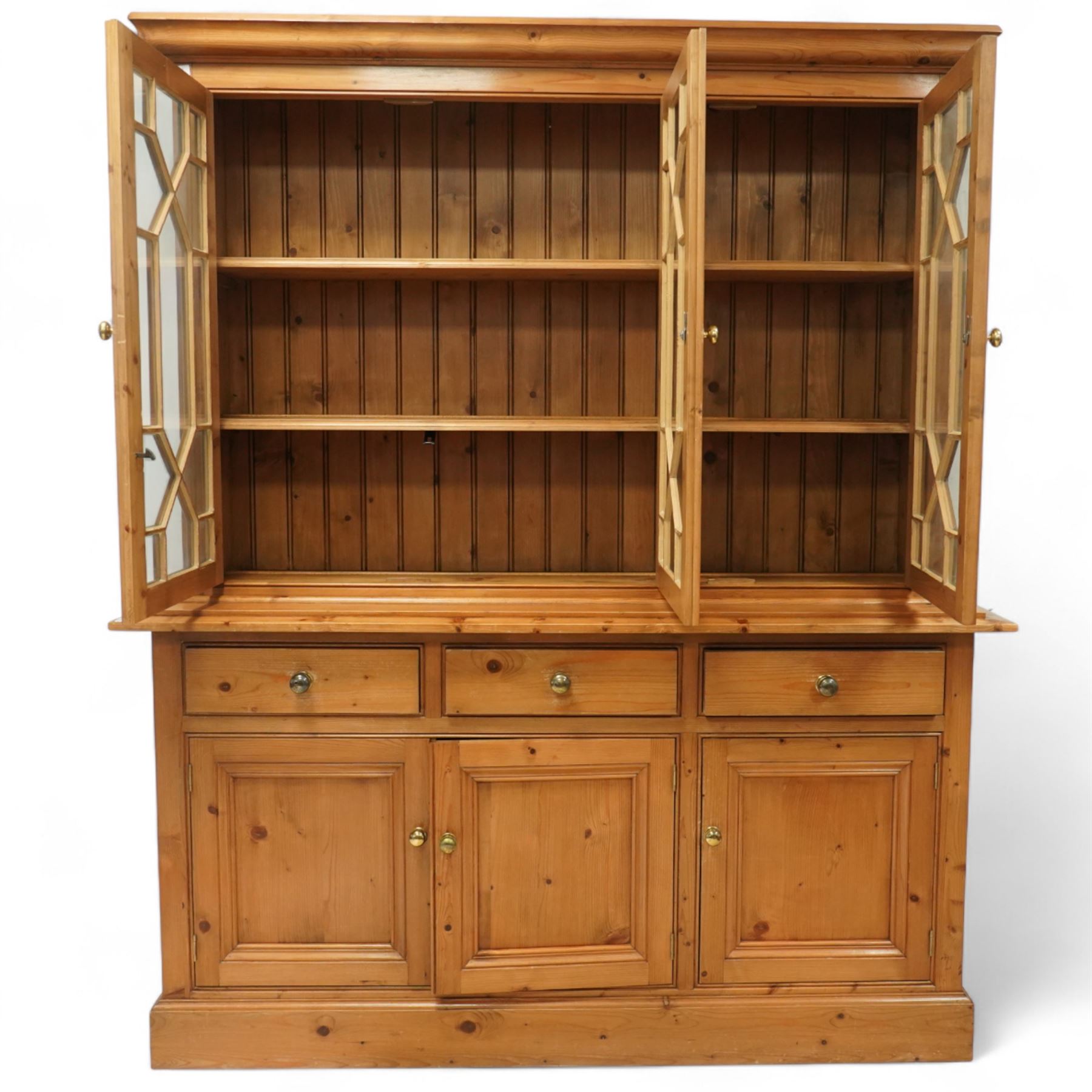 Mid 20th century pine glazed dresser on cupboard base, upper section of rectangular form with three astragal glazed hinged doors enclosing two adjustable wooden shelves and projecting frieze over three short drawers and three hinged panelled cupboard doors with brass handles, the front and sides, raised on a plinth base 