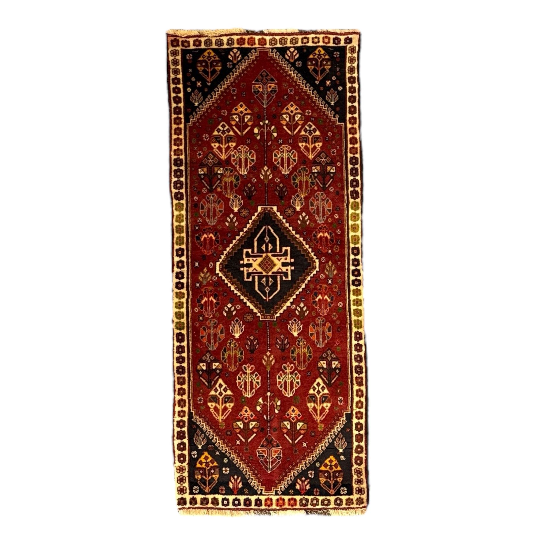 South West Persian Qashqai rug, hand knotted wool with central dark blue lozenge medallion containing geometric motifs, on a madder red field decorated with stylised floral boteh motifs, indigo spandrels, multiple borders of floral rosettes, from the region of Fars, south-west Persia