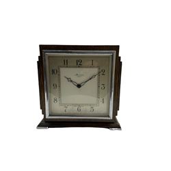 An Art Deco mantle clock retailed by Kendal & Dent London, in a square oak case on raised feet, chrome inset bezel and glass with a square chapter and Arabic numerals, minute track and pierced steel hands, timepiece movement with an integral key, wound and set from the rear.
H19 W19 D9
