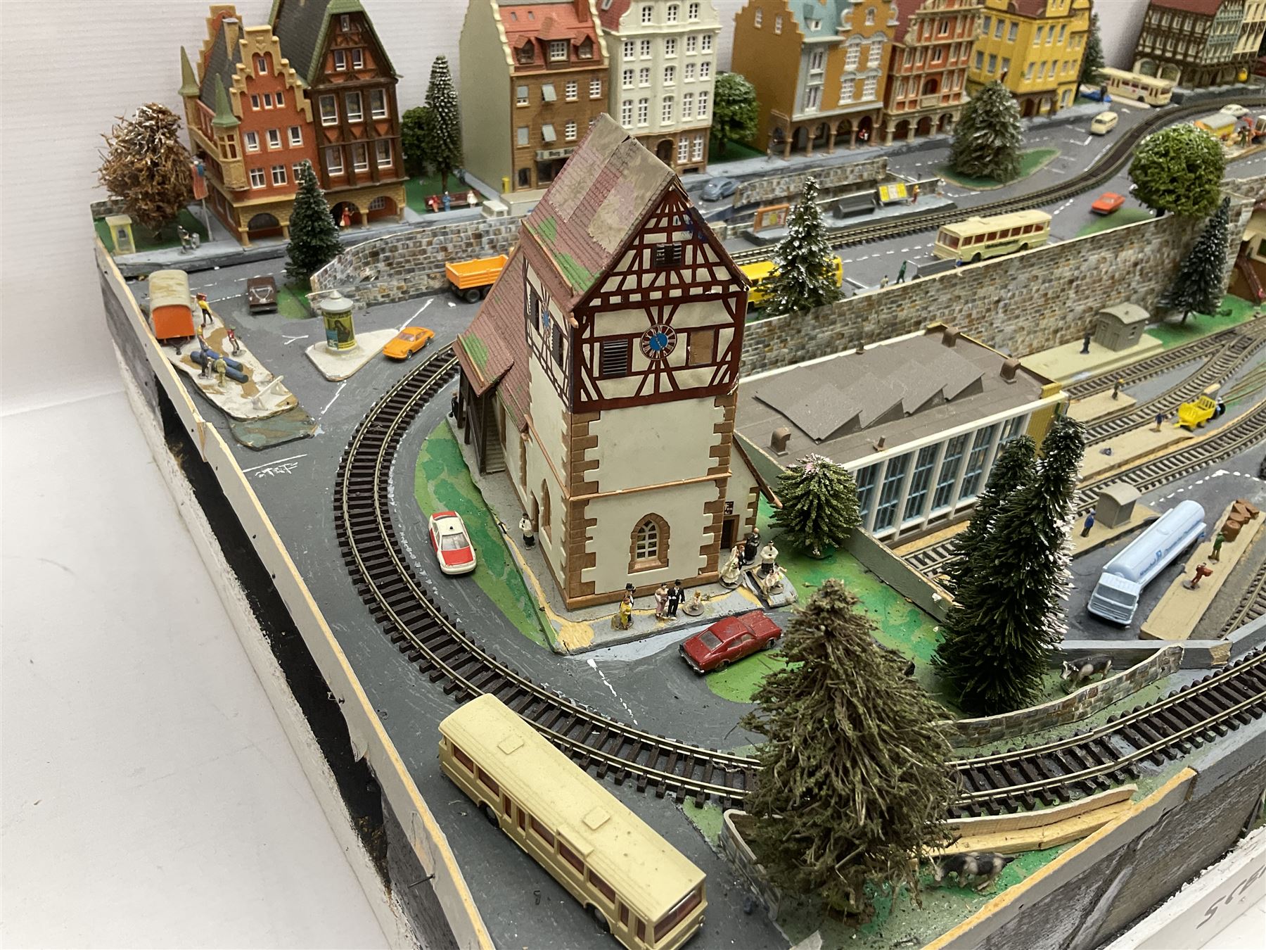 Table top 'N' gauge continental scenic layout as a split level town with various loops of track, station with numerous platforms, engine shed, assorted buildings, roads with motor vehicles and figures, tunnels, trees, river with bridge, tram depot etc 122 x 52cm