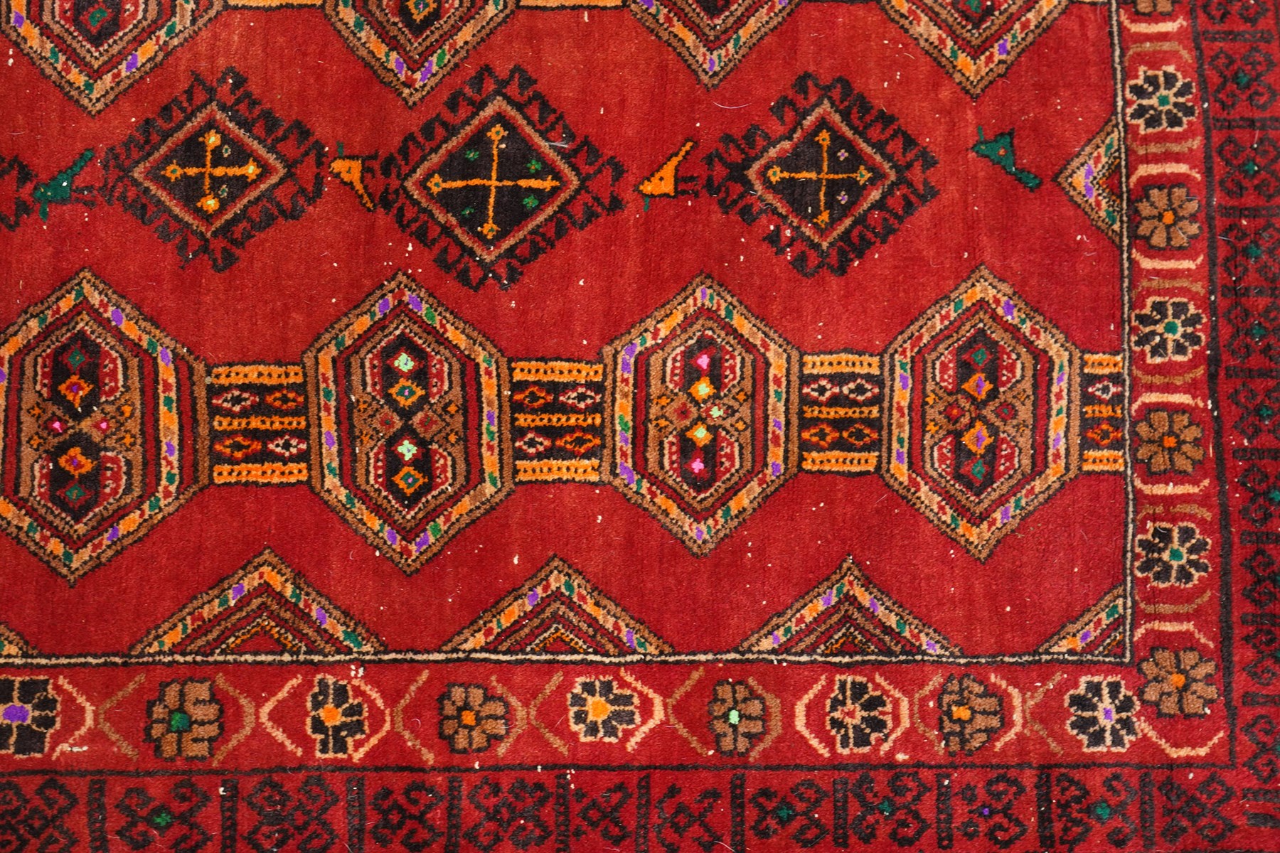Persian Baluchi crimson ground rug, decorated with three columns of geomtric motifs