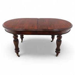 Victorian mahogany extending dining table, rounded rectangular top with moulded edge, pull-out action fitted with two additional leaves, raised on four reeded and fluted baluster legs with brass caps and castors