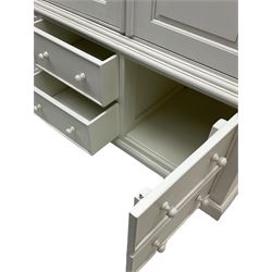 White painted triple wardrobe, projecting moulded cornice over three panelled doors, the interior fitted with hanging rails, four drawers and hinged cupboard to base, on bracket feet