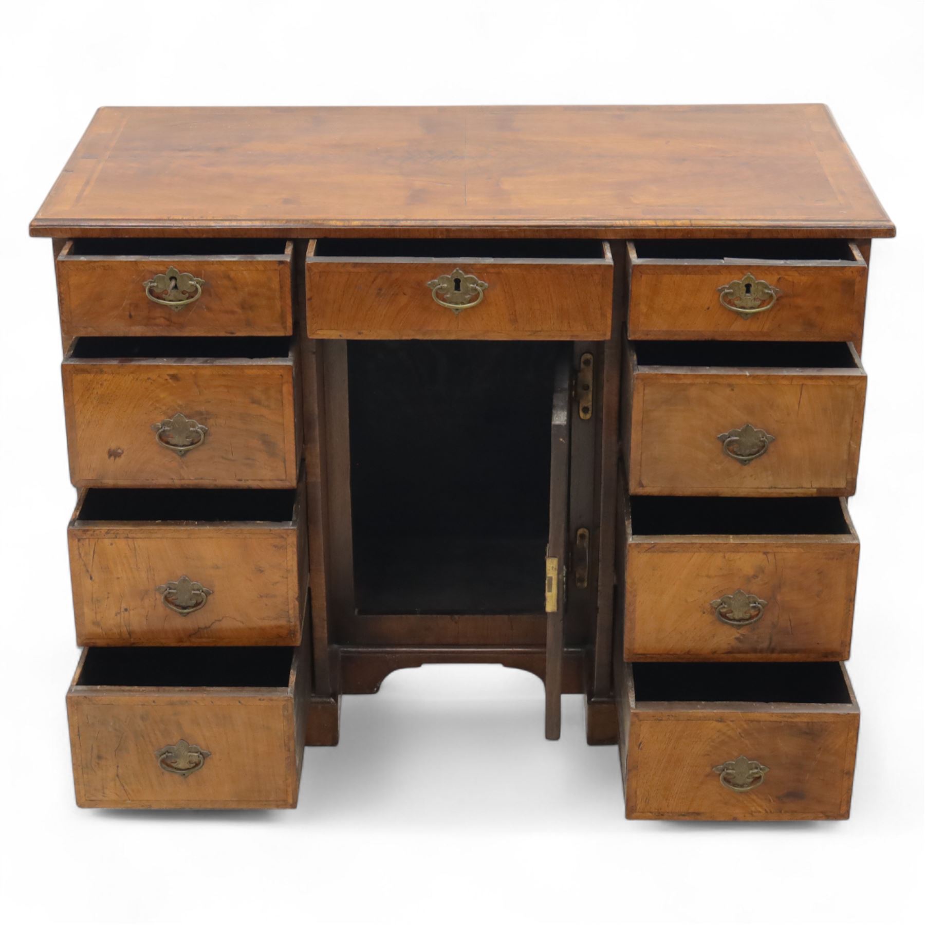 Early 20th-century Georgian-style walnut kneehole desk, the rectangular top with feather cross-banded border, above an arrangement of eight short drawers flanking a central cupboard door, fitted with brass backplate handles, raised on bracket feet