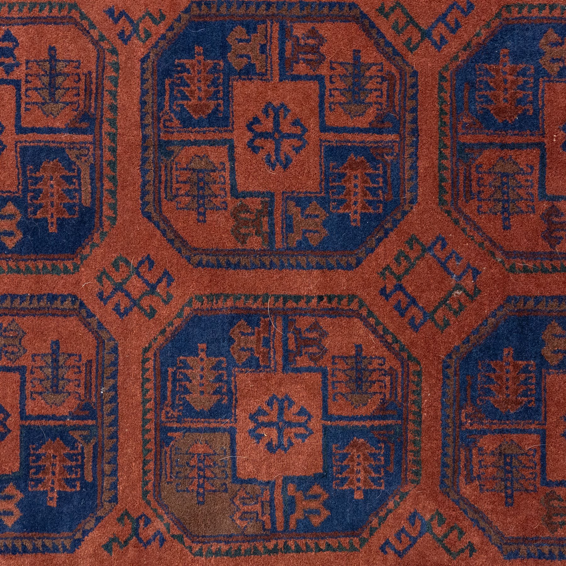 South East Persian Afshar hand-knotted rug, red ground decorated with a geometric design of octagonal medallions and incorporating stylized motifs in tones of indigo and dark brown within geometric borders, with fringe ends  