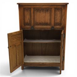 Old Charm - carved oak bar with three bar stools and associated Old Charm drinks cabinet, carved top with channels for glassware beneath, bar surface above glazed panels, shelves for glassware to the back, associated Old Charm drinks cabinet with fall front linenfold carving, above twin doors with shelved interior