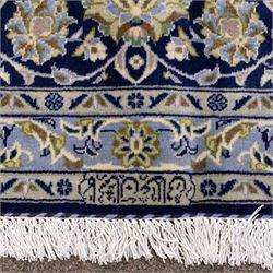 Central Persian Kashan hand-knotted rug, deep blue all-over field, finely decorated with dense scrolling floral sprays, palmettes, and flowering vines in ivory, soft gold, and pale green tones, enclosed by a multi-band floral border with corresponding guard stripes, with cotton fringe ends, signed Shah Abassi Workshop 