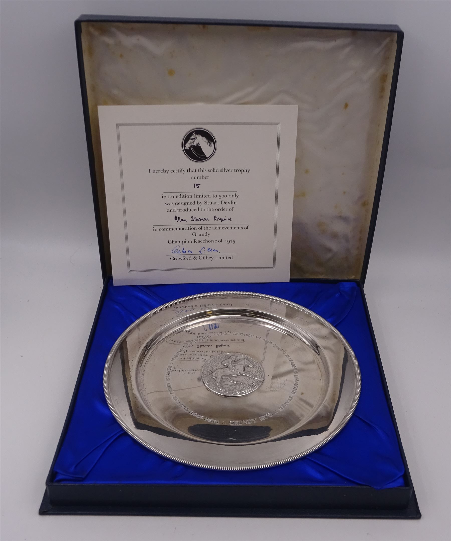 Modern limited edition silver salver, celebrating the achievements of Grundy, champion racehorse of 1975, each of circular form with gadrooned rim and plaque to centre depicting jockey mounted upon Grundy, designed by Stuart Devlin, limited edition no. 15/500, hallmarked London 1976, makers mark LH, D23cm, within silver lined fitted box and limited edition certificate 