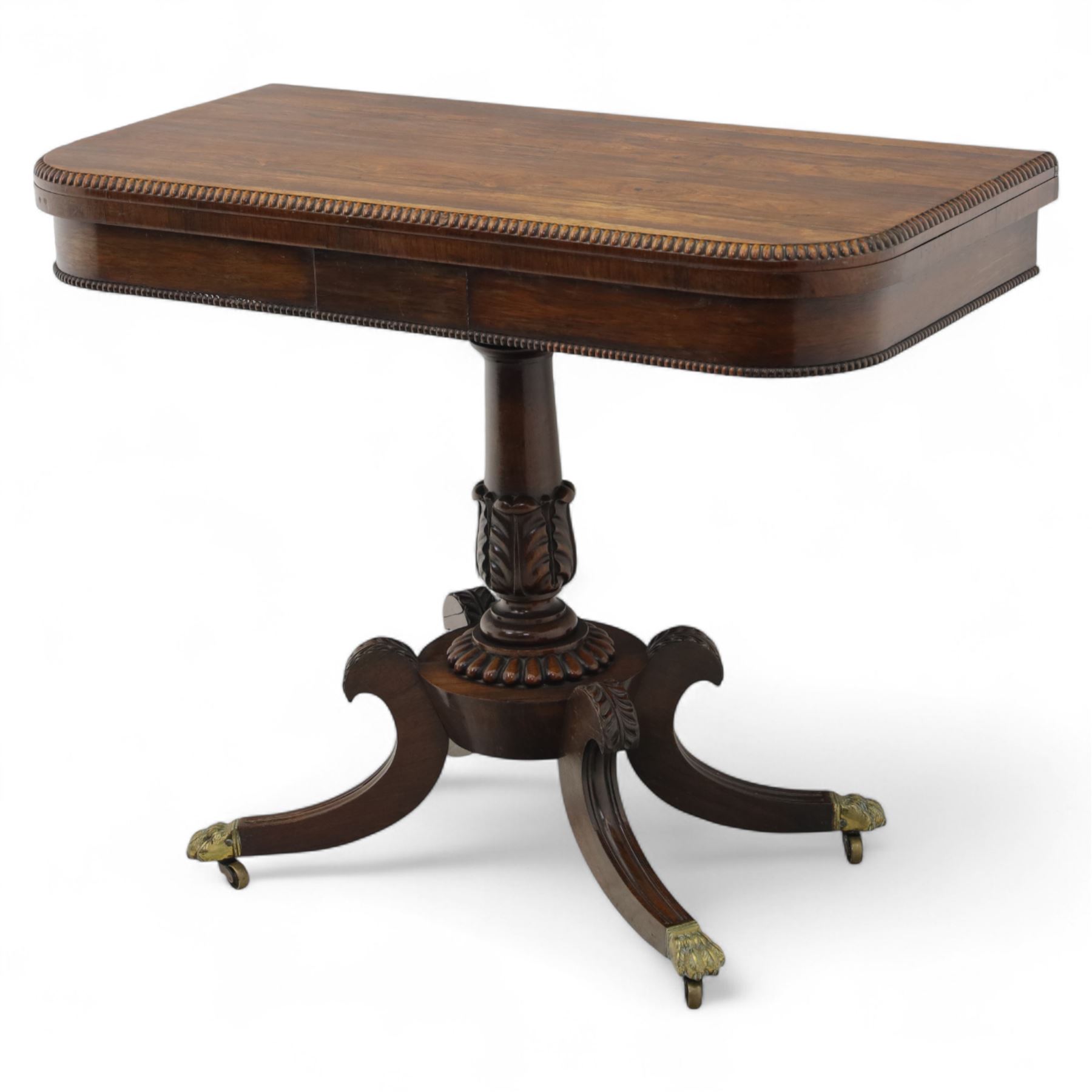 Regency rosewood fold over card table, the rectangular top with rounded corners and gadrooned edge opening to reveal a green baize lined interior, raised upon convex lobbed and acanthus pedestal and four fluted sabre legs, terminating in brass lion paw feet and castors