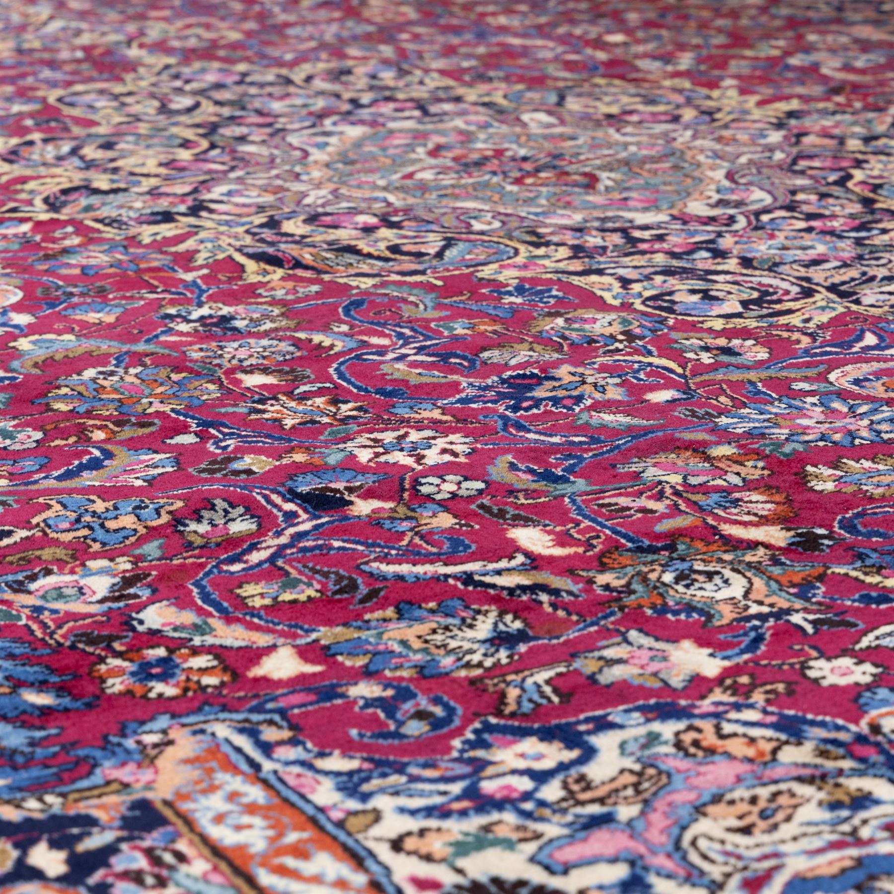 Large North East Persian Meshed hand-knotted carpet with signature, raspberry red field with central shaped cusped medallion, densely decorated with intricate arrangement of scrolling vines, and florals designs within conforming spandrels and a dark ground border richly ornamented with stylized flowers, vase and bird ornamentation, enclosed by guard stripes, with cotton fringe ends
