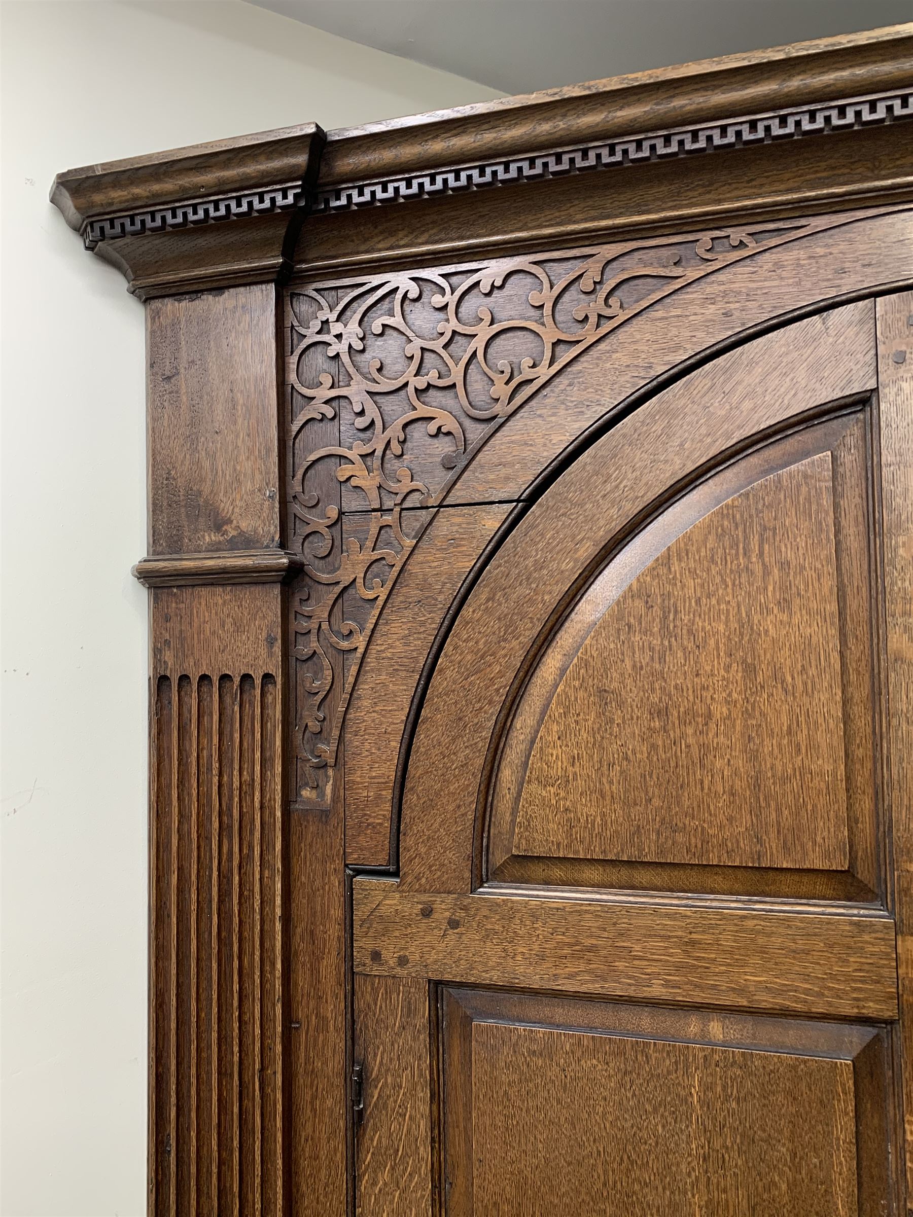 Large George III oak corner cupboard, projecting cornice over two stepped arch doors with fielded panels and blind fret work spandrels, flanked by fluted uprights, cupboard below enclosed by two fielded panel doors, the painted interior fitted with shaped shelves
 