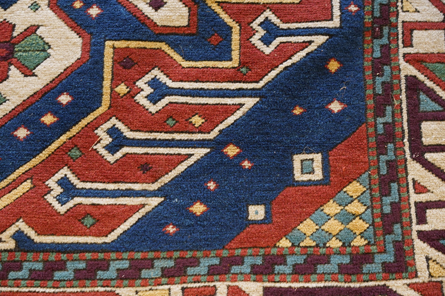 Caucasian Kazak indigo and vermillion ground rug, the geometric field boldly woven with two medallions interspersed with symbolic tribal motifs and shapes, with contrasting ivory guard band