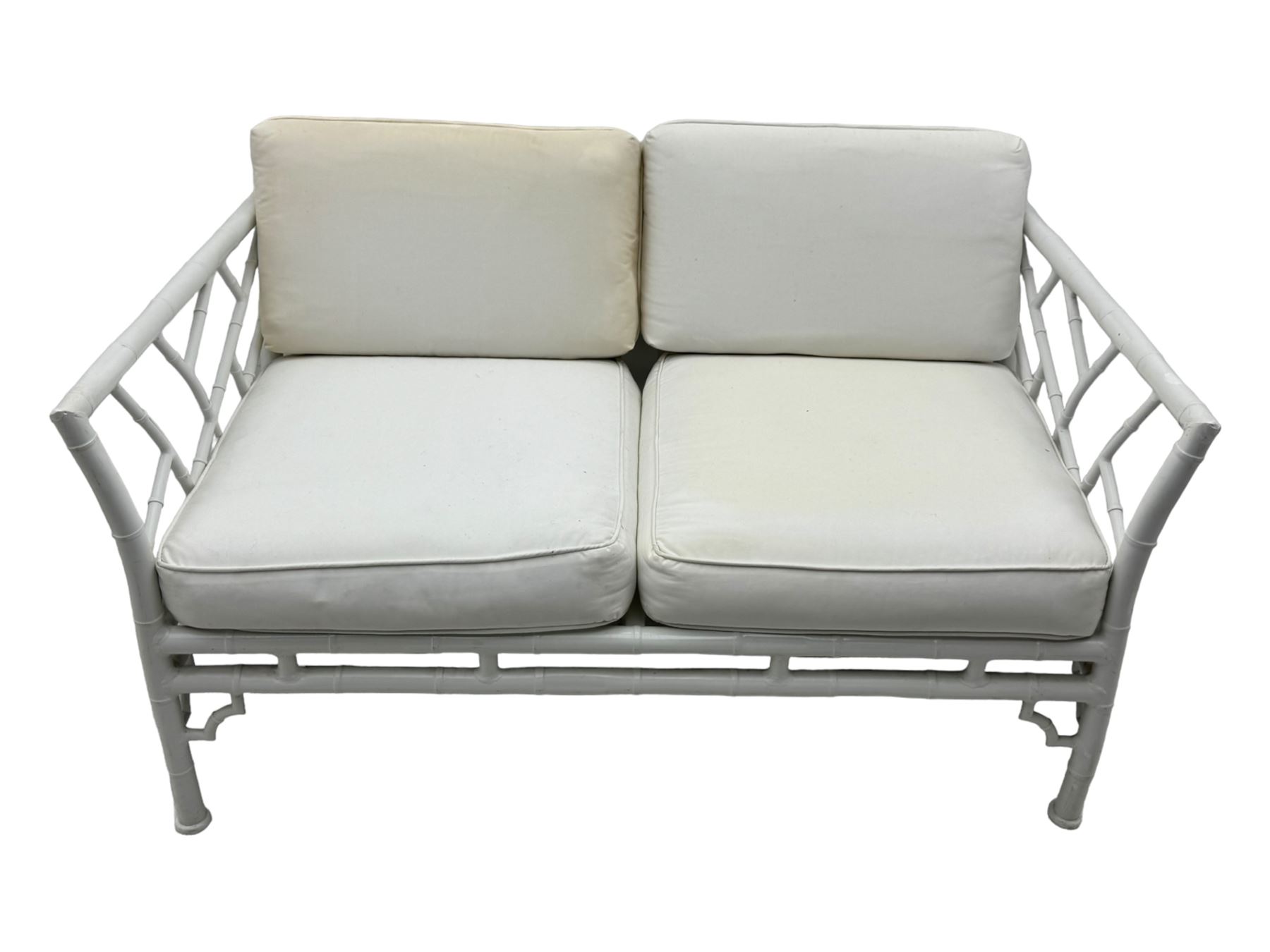 Late 20th century faux bamboo conservatory sofa, white painted frame with geometric openwork back and sides, loose cream cushions, on cylindrical supports (W134cm, D76cm, H80cm); matching armchair (W75cm, D76cm, H80cm); matching coffee table with glass insert (W46cm, D45cm, H36cm)