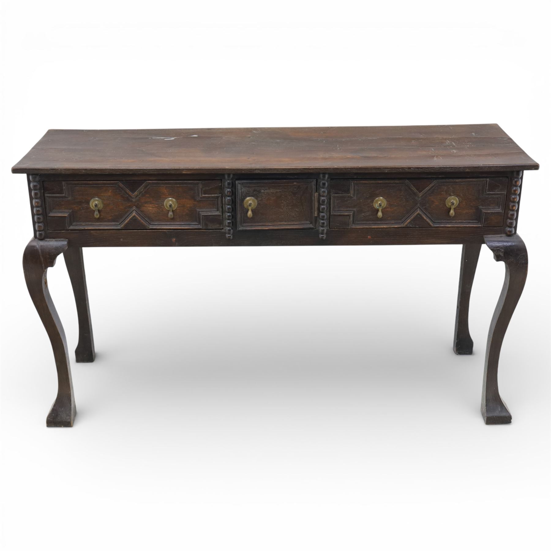 Late 19th century Jacobean revival oak side table, plank top with moulded edge over a central cupboard door and two frieze drawers carved with geometric lozenge motifs and framed by bobbin turned uprights, fitted with brass drop handles, raised on shaped cabriole supports with block feet