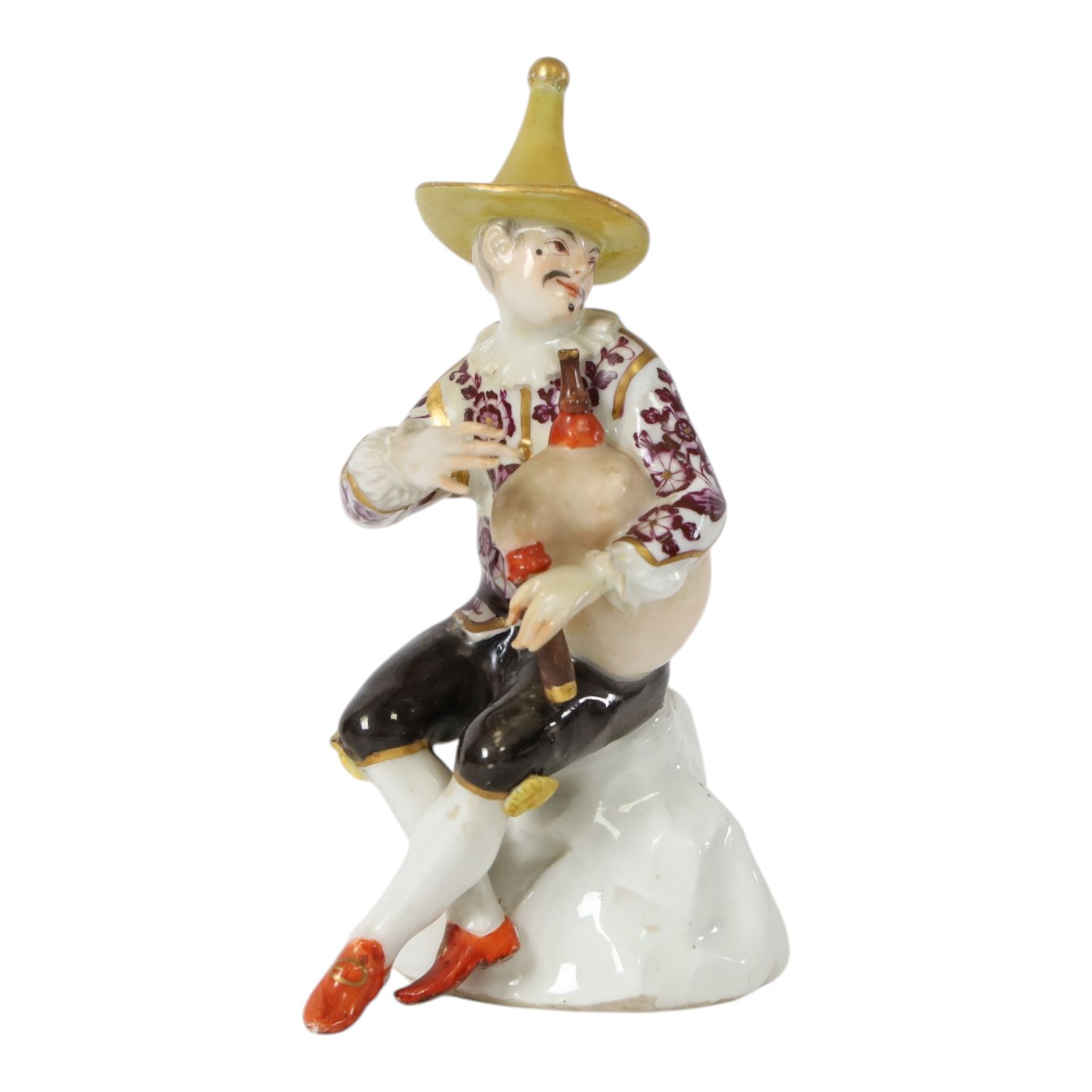 Mid 18th century Meissen figure, modelled as a harlequin playing bagpipes, circa 1745, possibly modelled by J.F.Eberlein after earlier models by J.J.Kändler, wearing a gilt edged tunic painted with flowers, black breeches with rosettes at the knees, red shoes and conical yellow hat, seated upon a rock, with traces of blue crossed swords mark beneath, H14cm