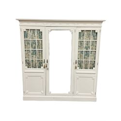 Maple and Co - Edwardian Hepplewhite design white painted triple wardrobe, foliate carved projecting cornice over ribbon and husk swag decorated frieze, two curtain lined astragal glazed doors and centre full mirror door, fitted mahogany interior including slides and drawers, plinth base, label to top of central door