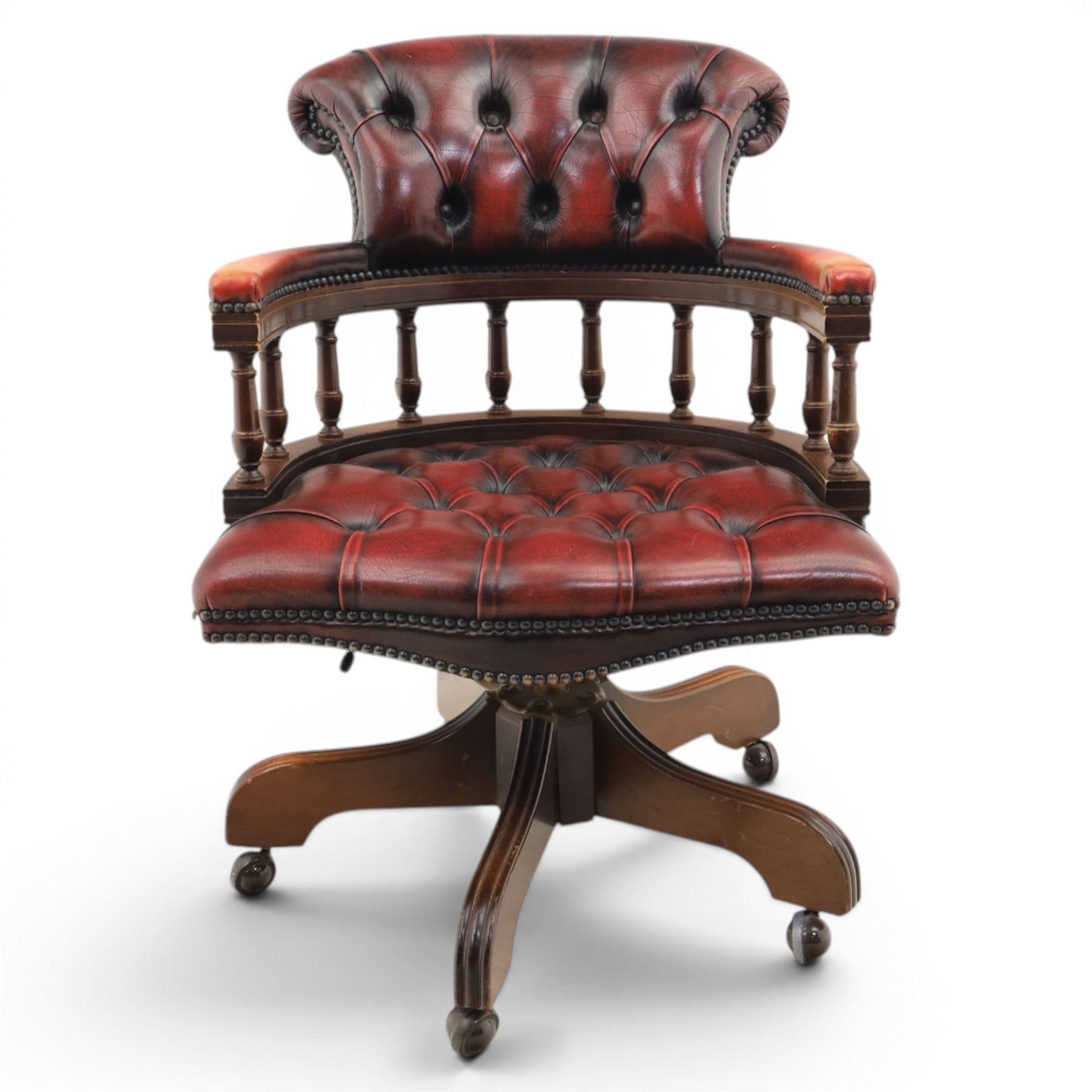 Captains swivel desk chair upholstered in oxblood leather, buttoned back and seat, shaped arm bow raised on turned spindles, five spoke base raised on castors